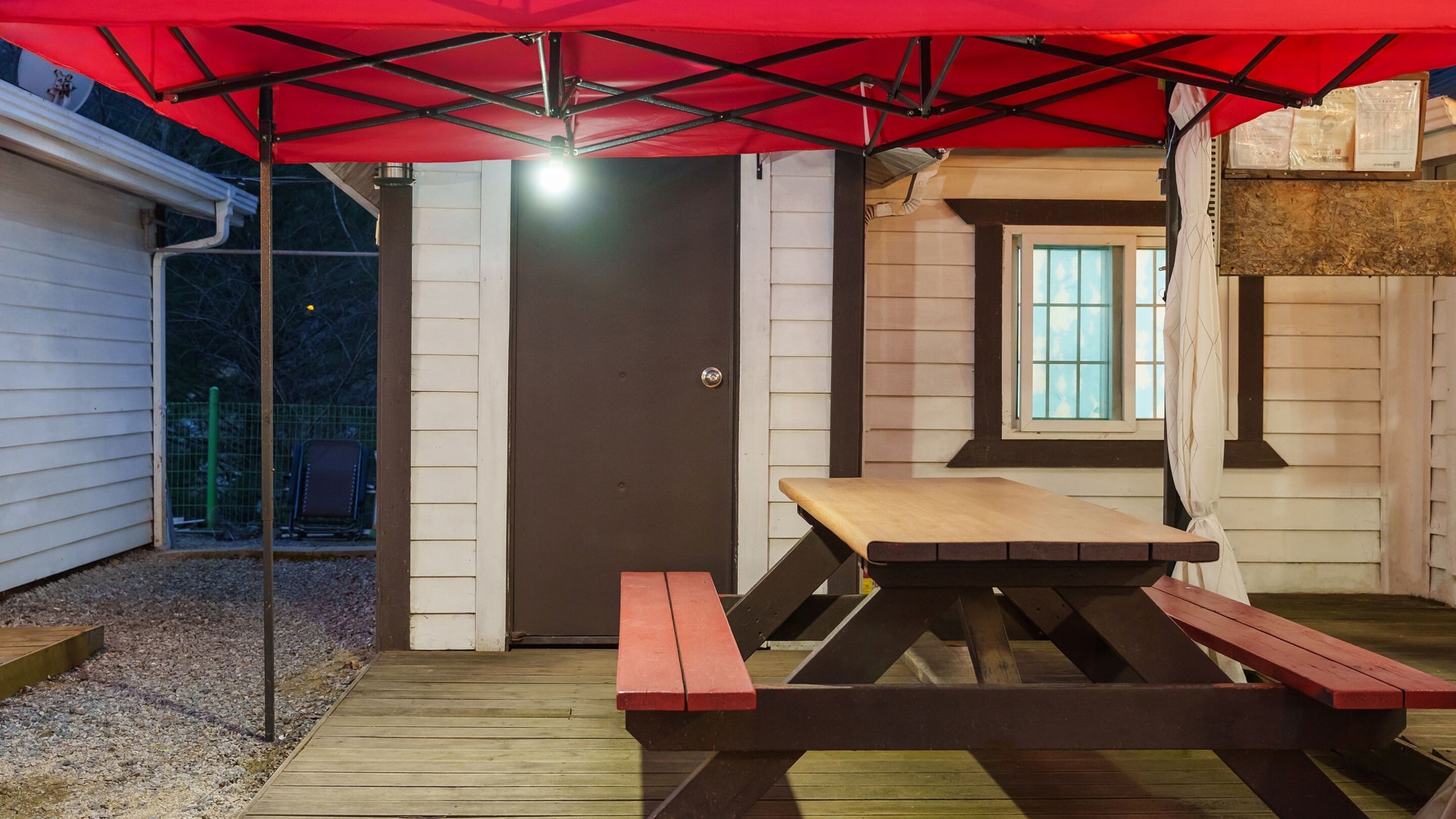 Un espacio al aire libre techado con una mesa de picnic y bancos, una puerta y una ventana.