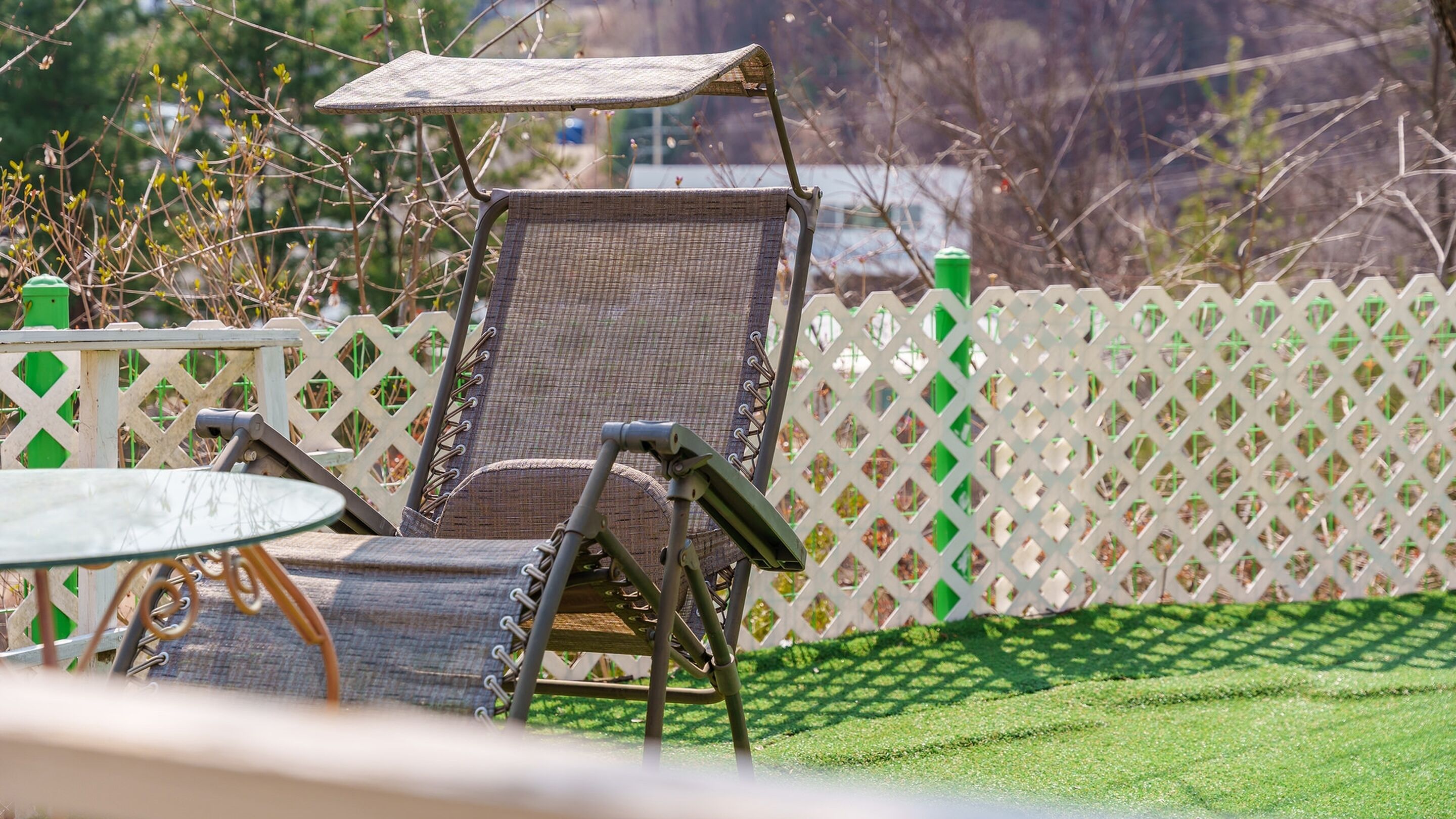 A patio area with a wicker chair, a small table, and a white lattice fence.