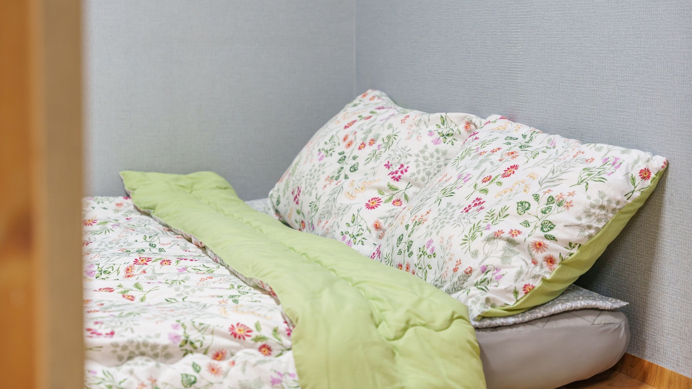A neatly made bed with floral bedding and a green throw blanket.