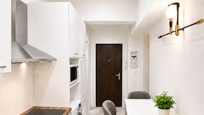 A compact kitchen with a wooden countertop, built-in appliances, and a dining area with chairs and a table. - Metropole Apartments Romana Square (Bucharest)