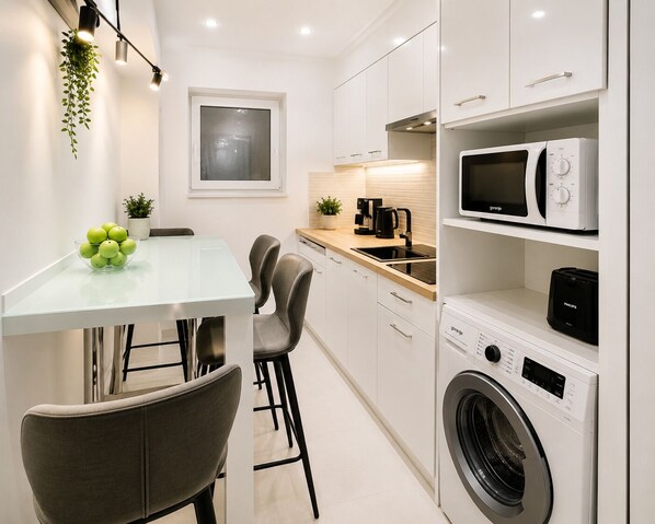 A modern kitchen with white cabinets, a built-in washing machine, a microwave, and a coffee maker.