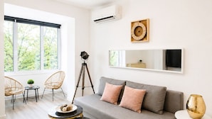 A modern living room with a grey sofa, two armchairs, a tripod floor lamp, a round table with a plant, and a round table with a decorative vase. - Metropole Apartments Romana Square (Bucharest)