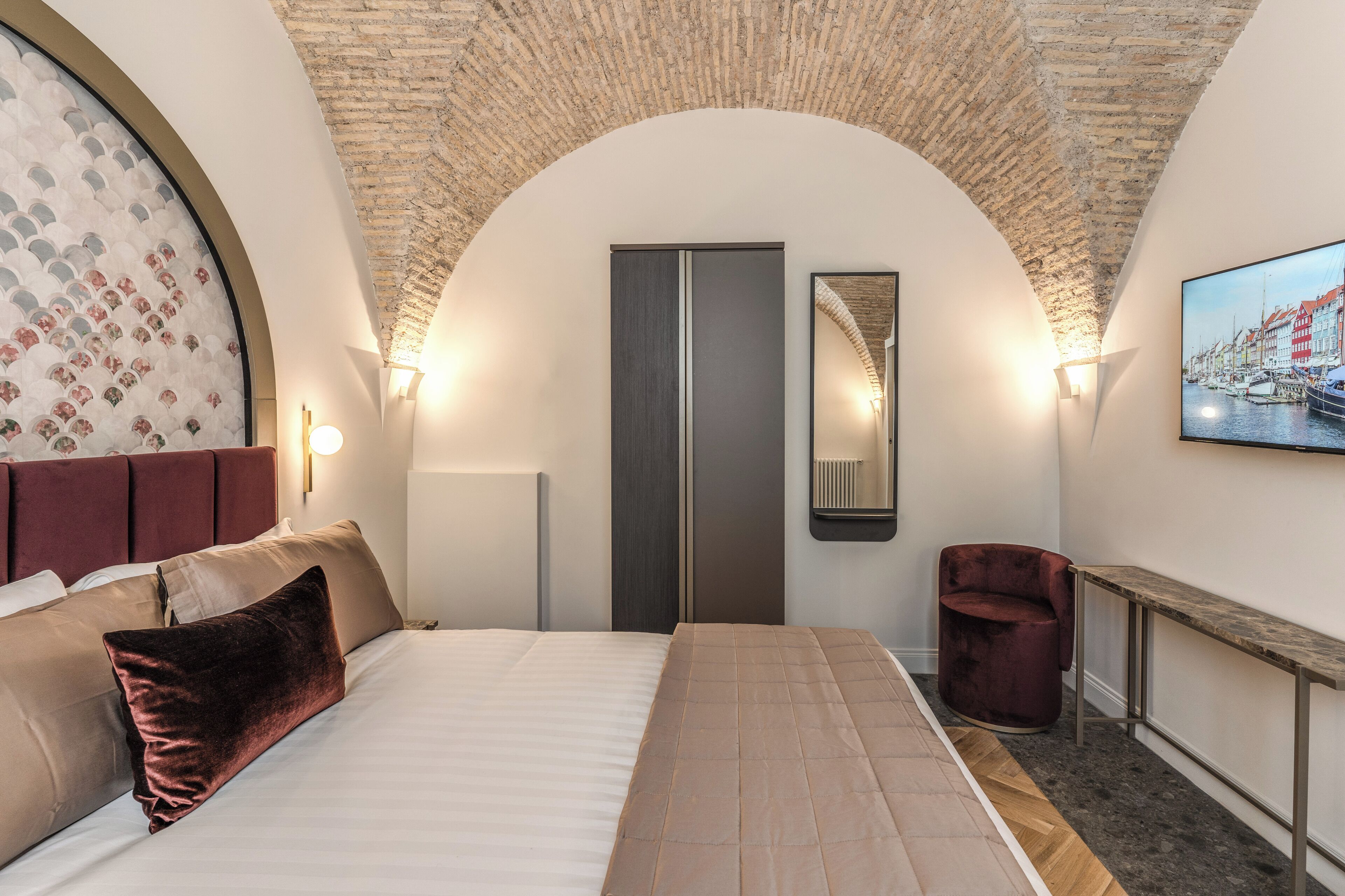 Een slaapkamer met een groot bed, een rode stoel, een spiegel en een schilderij aan de muur.