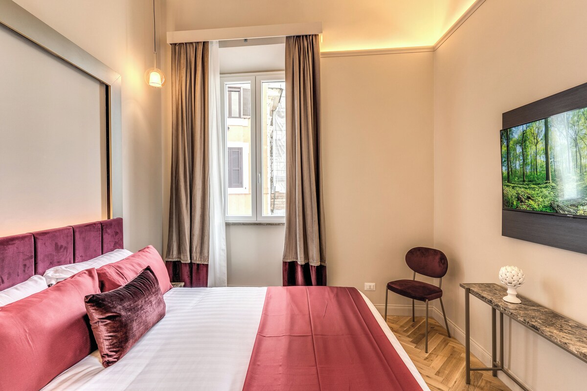 Una habitación de hotel con cama, una silla, una mesita y un cuadro en la pared.