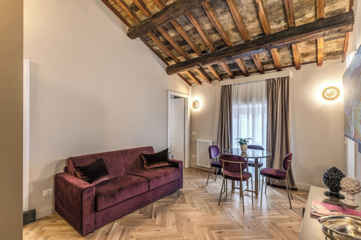 Una sala de estar con techo de madera, un sofá rojo, una mesa de comedor con sillas y una ventana con cortinas.