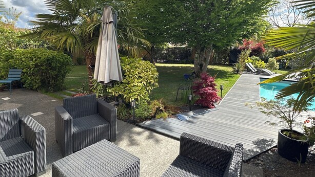 An outdoor patio area with wicker furniture, a pool, and a variety of plants. - Room in contemporary house with swimming pool (Le Mans)