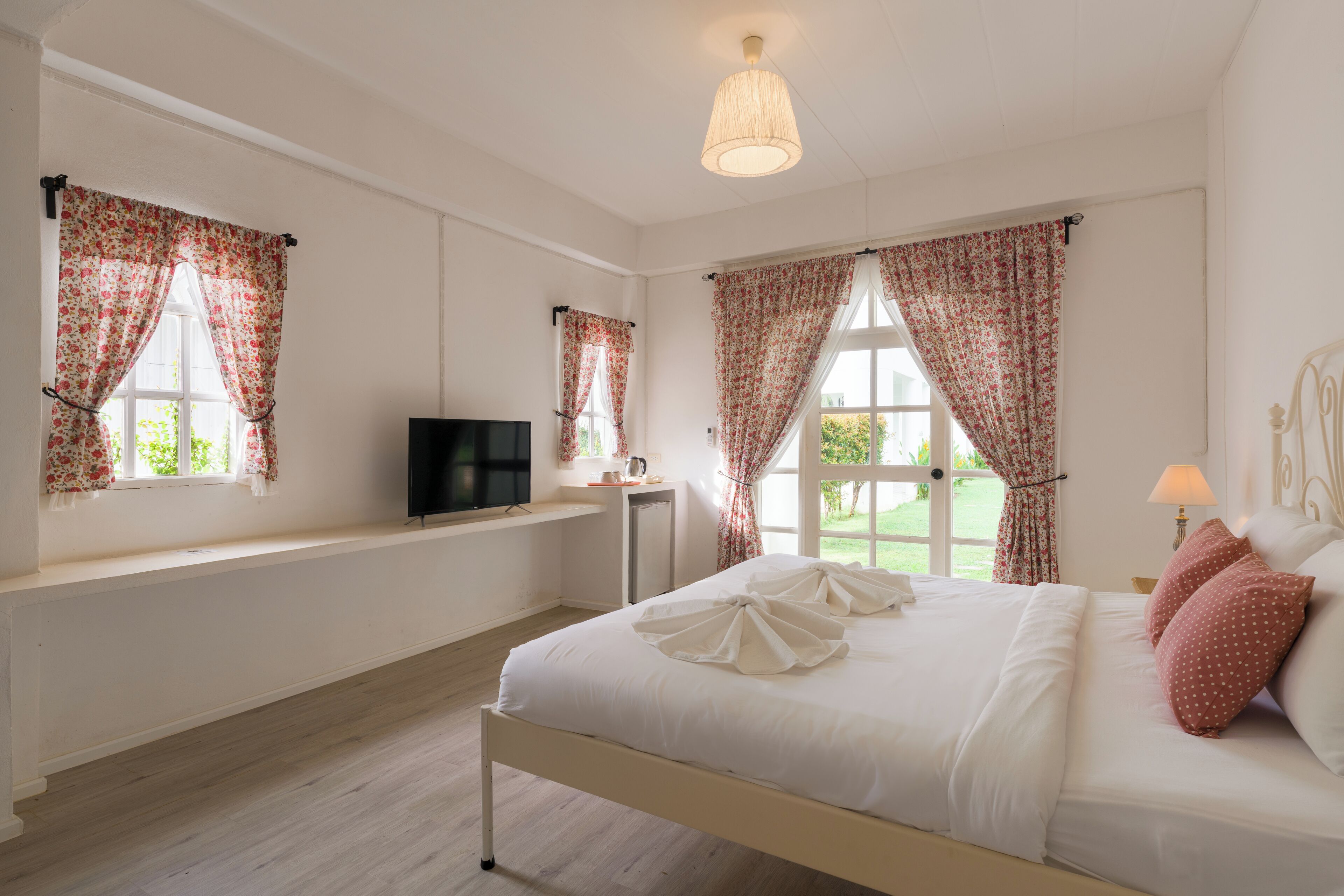 A bedroom with a bed, a television, a window with curtains, and a lamp.