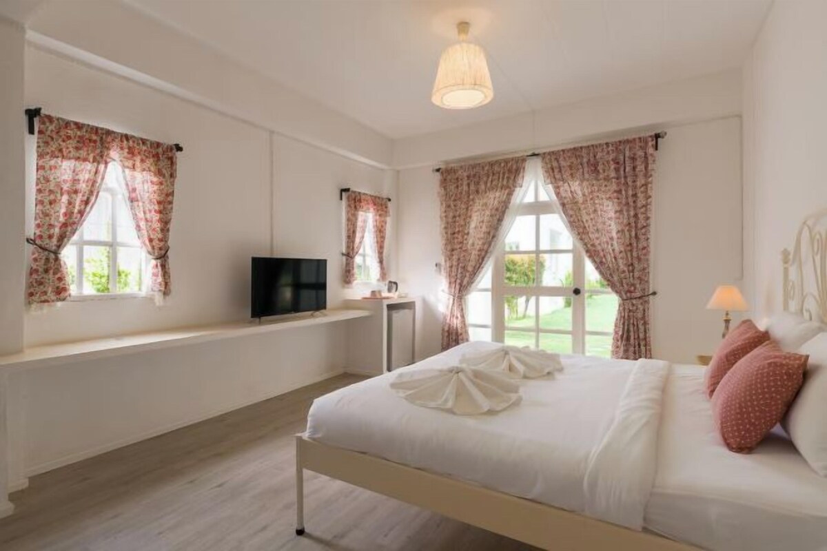 Un dormitorio con cama, televisión, ventana con cortinas y lámpara.