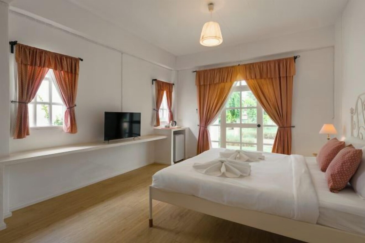 Un dormitorio con cama, televisión, escritorio y ventana con cortinas.