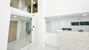 Quarto de hotel moderno e minimalista com porta de vidro para uma varanda, piso de mármore e balcão de recepção em mármore.