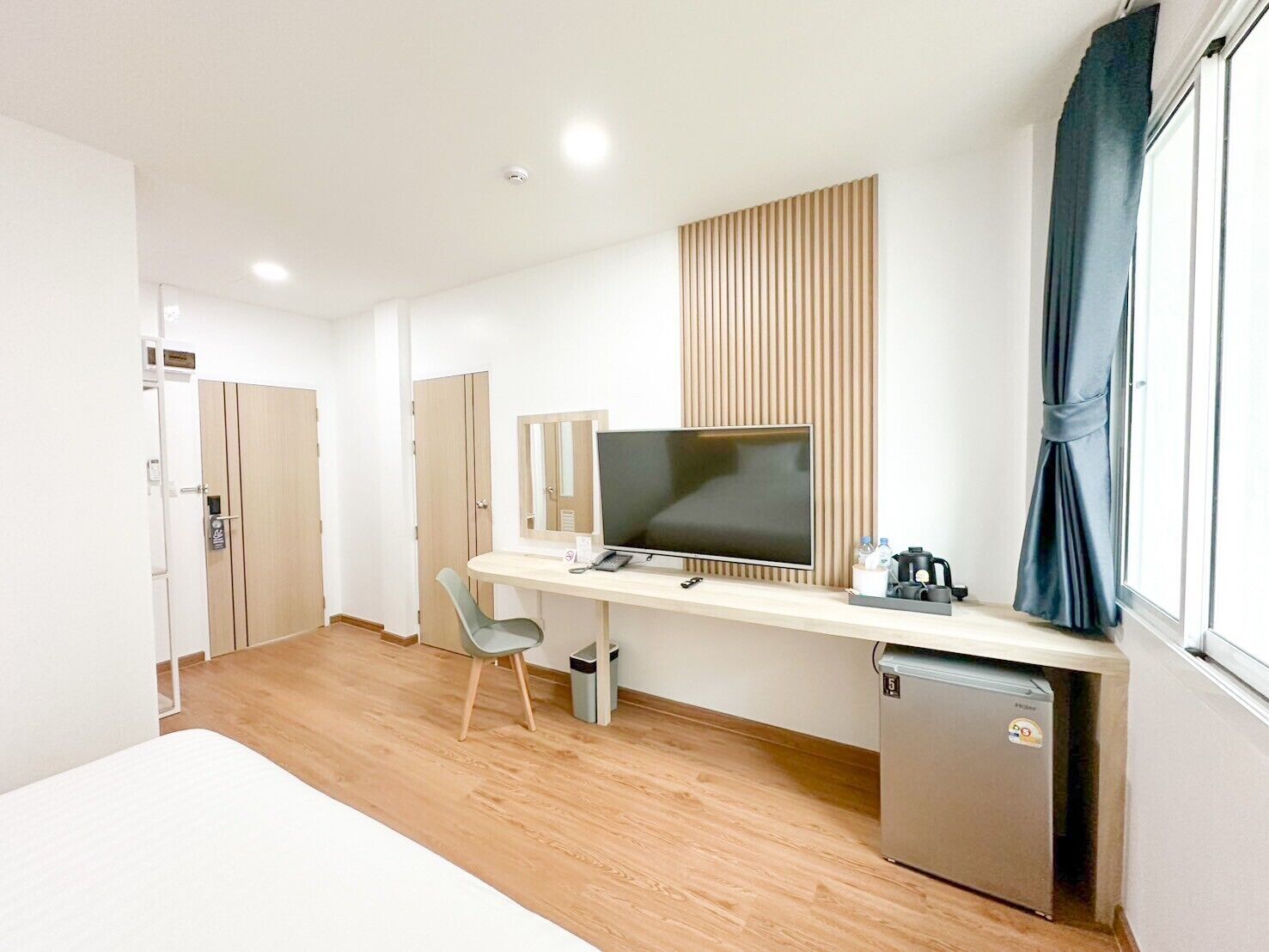 Ein modernes Hotelzimmer mit Schreibtisch aus Holz, einem Flachbildfernseher, einer kleinen Kühlschrank und einem Fenster mit Vorhängen.