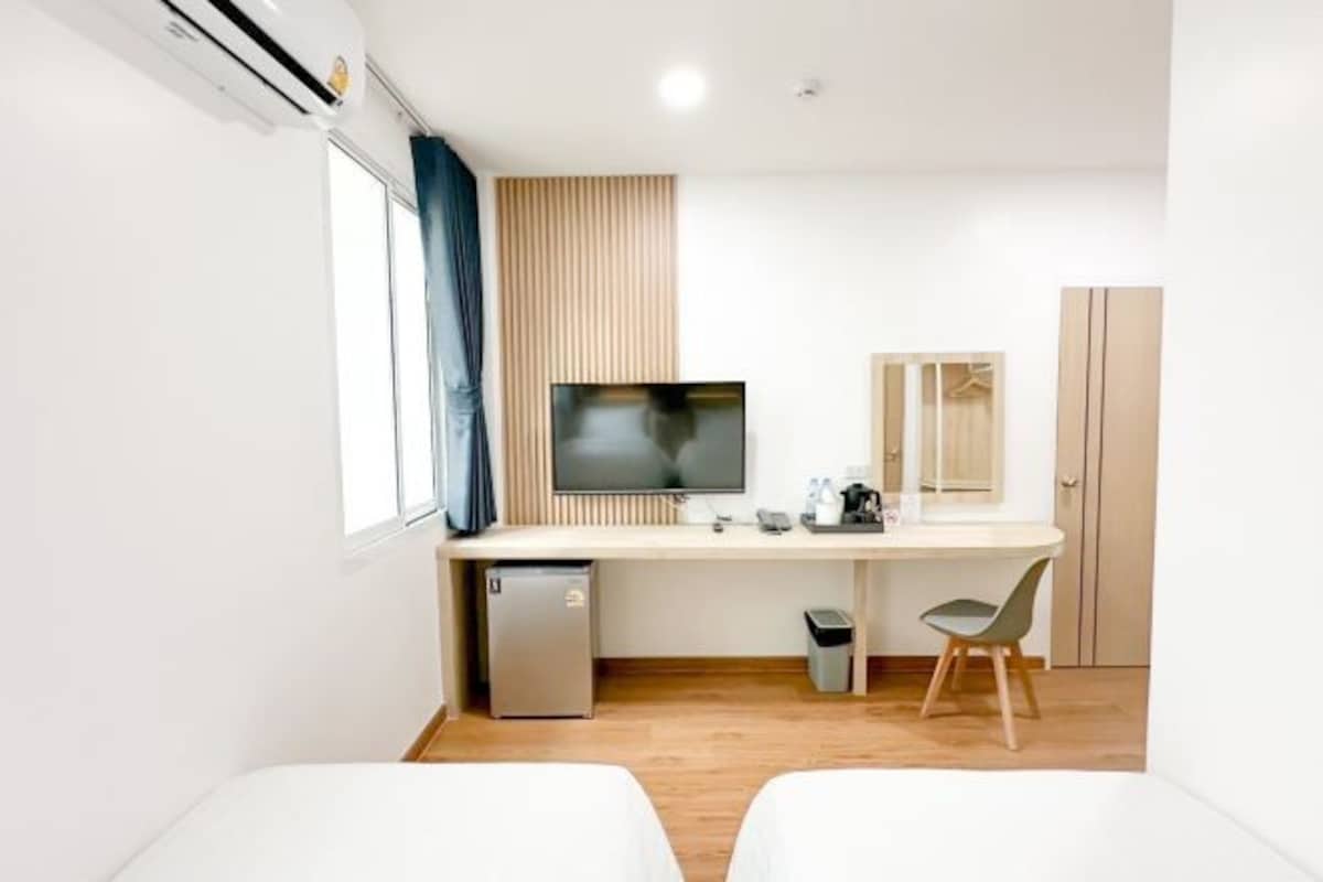A hotel room with a bed, a desk with a computer, a TV, and a small fridge.