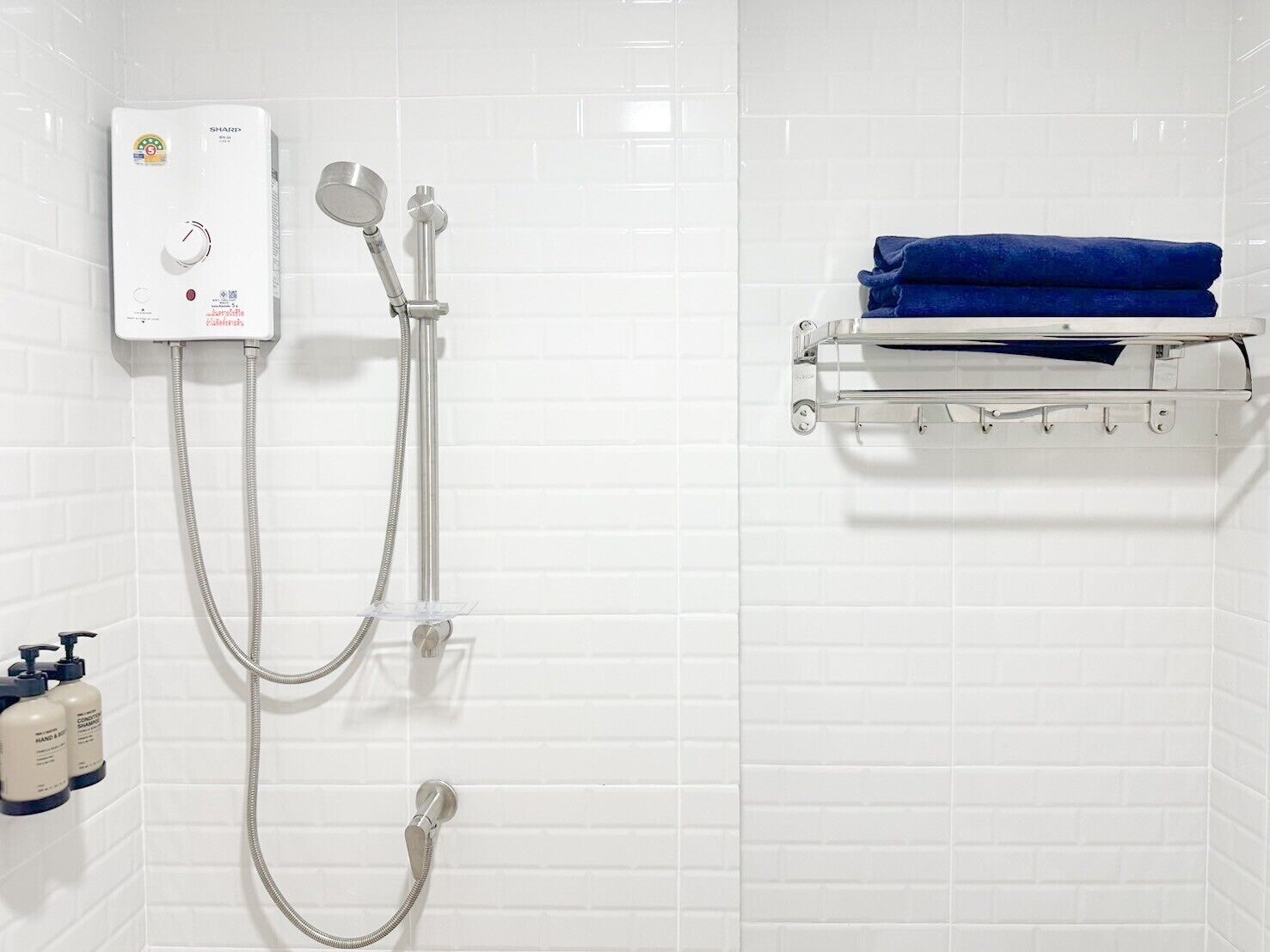 A bathroom with a white tiled wall, a handheld showerhead, a wall-mounted faucet, and a towel rack with a folded towel.