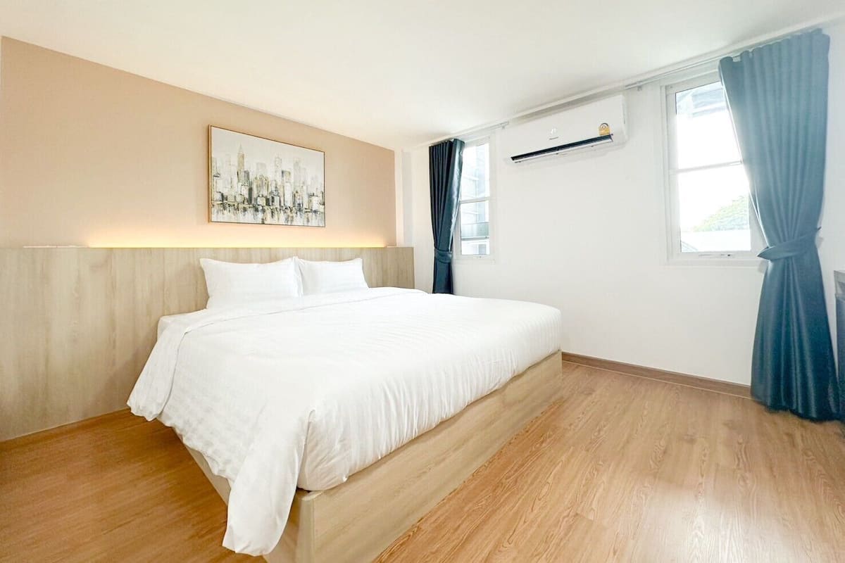 Een moderne slaapkamer met een groot bed, een stadsgezicht schilderij, een raam met gordijnen en een airconditioning.