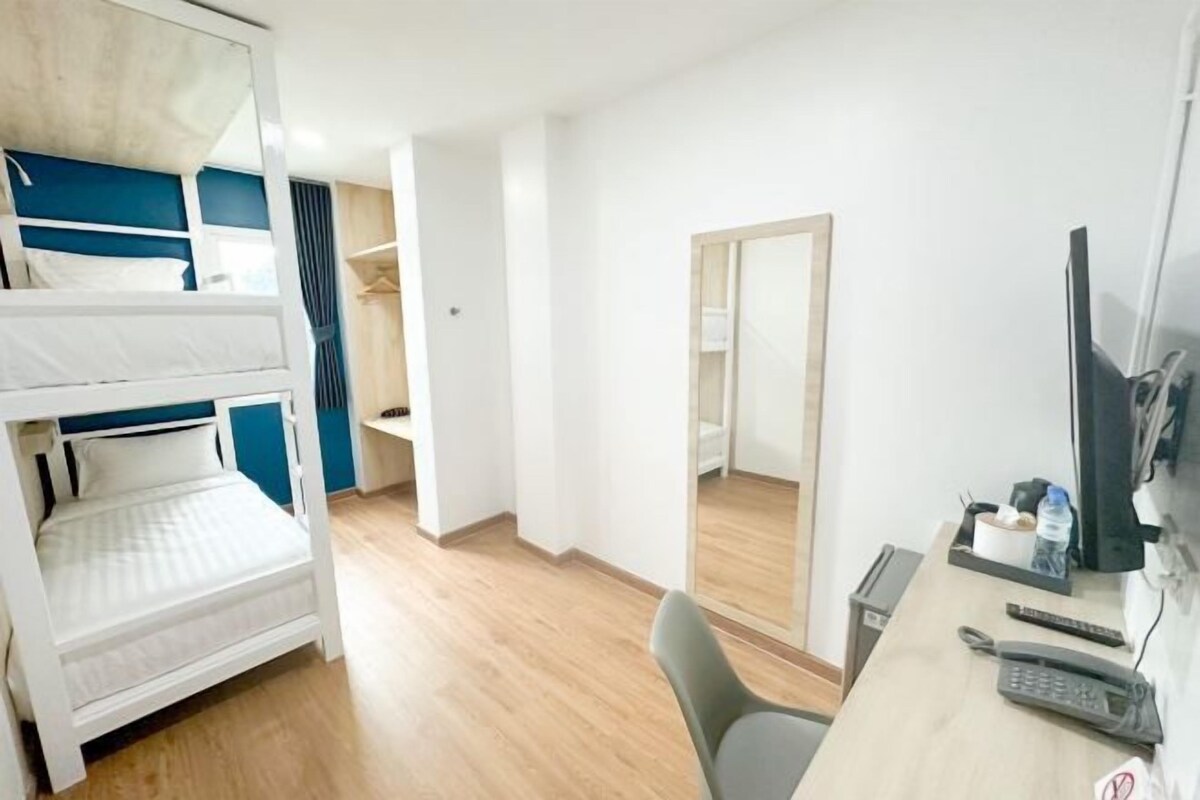 A hotel room with a bunk bed, a desk with a computer, a mirror, and a chair.