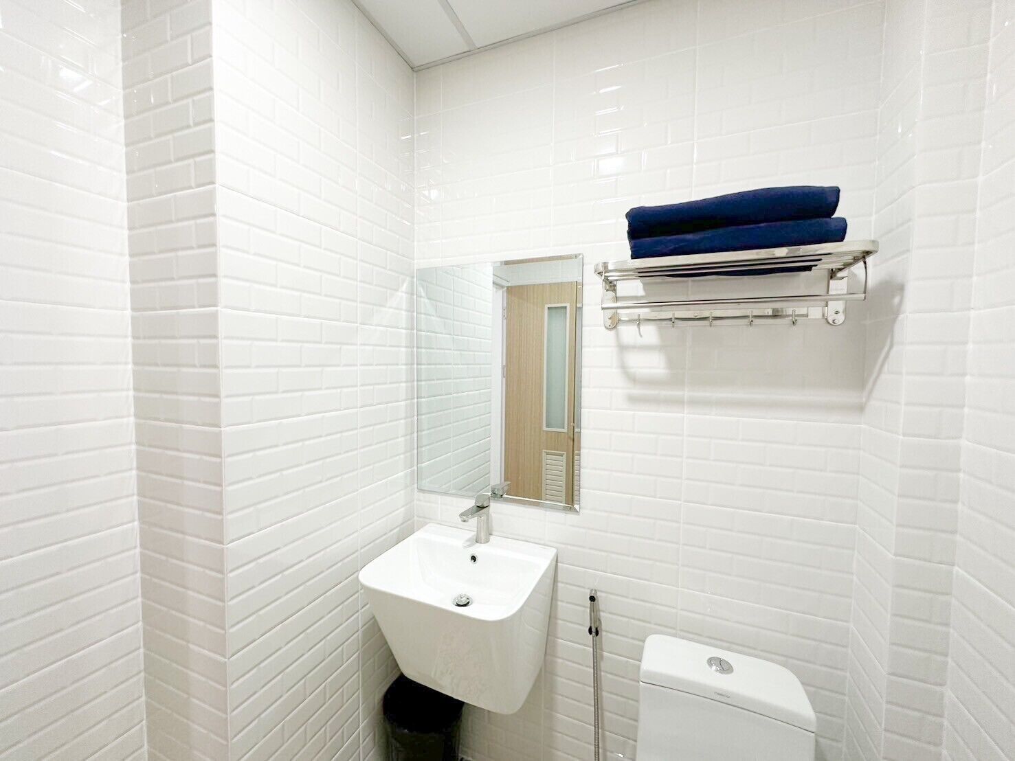 A bathroom with white subway tiles, a white sink, a mirror, a towel rack with blue towels, and a toilet.