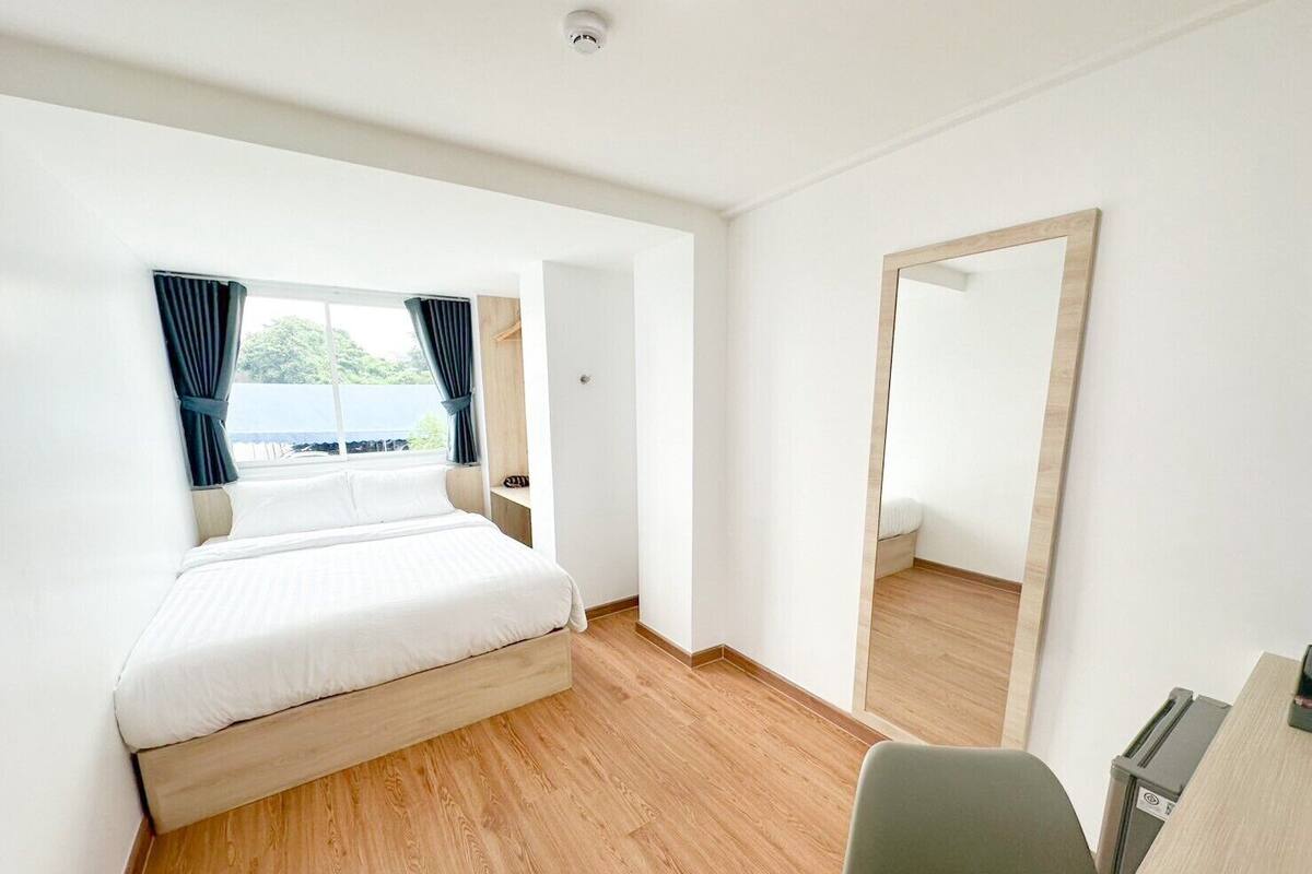 Een hotelkamer met een bed, een bureau, een stoel, een spiegel en een raam met gordijnen.