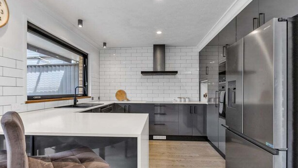 Una cocina moderna con azulejos blancos tipo metro, electrodomésticos de acero inoxidable y una zona de bar con una silla acolchada.