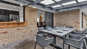 Un área de comedor al aire libre con pared de ladrillo, barra de madera y mesa preparada para cuatro.