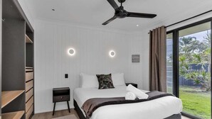 Un dormitorio moderno con una cama grande, un ventilador de techo, una mesita de noche y vistas al exterior.