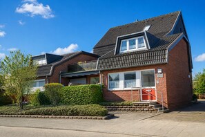 Une maison à deux étages, construite en briques, avec un toit en pente, une porte de garage bien visible et un petit jardin à l’avant.