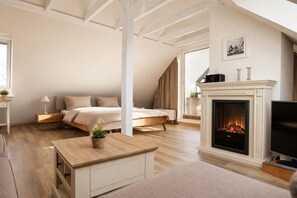 A bedroom with a bed, a bedside table with a lamp, a fireplace, and a television. - Vacation apartment in Cuxhaven Duhnen-Döse directly on the beach with balcony & beach chair (Cuxhaven)