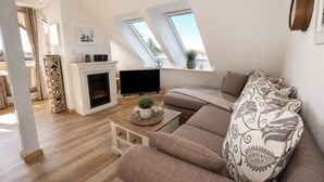 Ein modernes Wohnzimmer mit Kamin, Fernseher, Sofa und großen Fenstern.