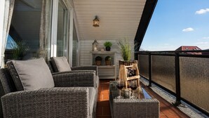 Ein Balkon mit Korbmöbeln, einem kleinen Tisch mit Weingläsern und einer Laterne.