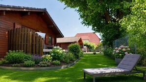 Une maison en bois avec un toit rouge, un jardin où poussent différentes plantes et un fauteuil de jardin.