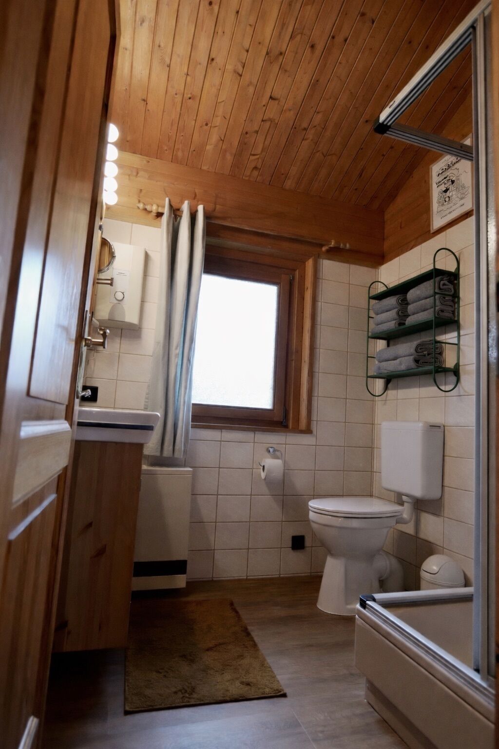 A compact wooden cabin bathroom with a toilet, sink, and shower area.