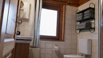 A compact wooden cabin bathroom with a toilet, sink, and shower area.