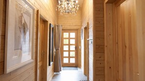 Un couloir en bois, orné d’un lustre, avec une porte dotée d’une fenêtre et un tableau encadré accroché au mur.