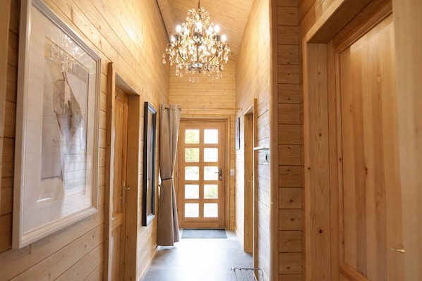 A wooden hallway with a chandelier, a door with a window, and a framed picture on the wall.