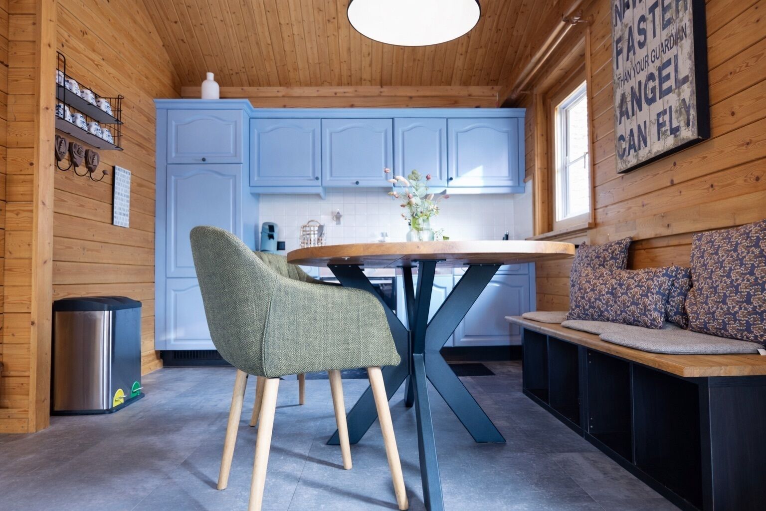 A cozy cabin interior with a dining table, chairs, a bench, and a kitchen area with blue cabinets.