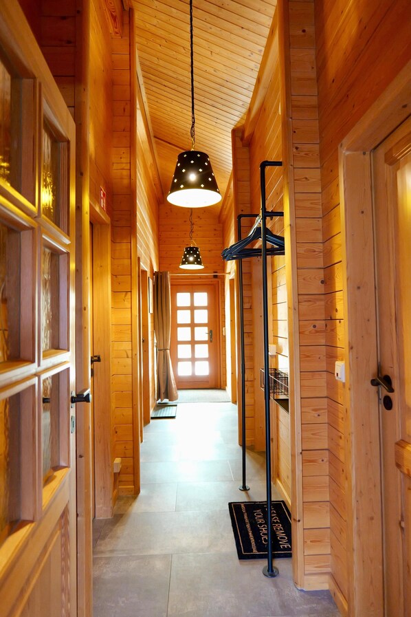 A wooden hallway with a hanging light fixture, a coat rack, and a door with a window.