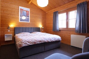 A wooden cabin bedroom with a bed, two bedside lamps, a window with curtains, and a poster on the wall. - Vacation home in Cuxhaven Berensch | Küstenhaus Kormoran (Cuxhaven)