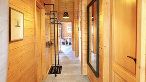 Un pasillo interior de madera con una lámpara en el techo, un perchero de metal negro y una puerta a la derecha.