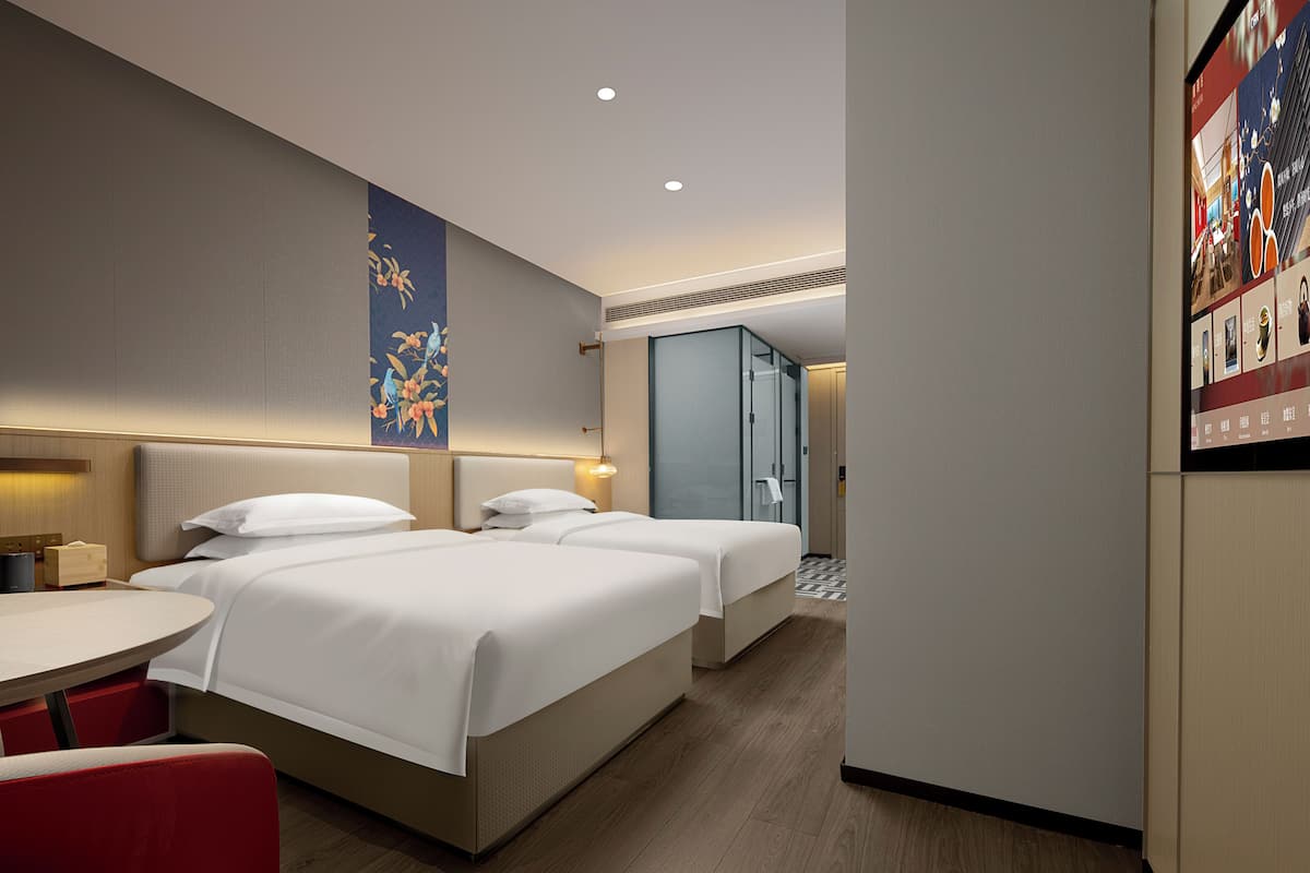 A hotel room with two beds, a small table, and a red chair.