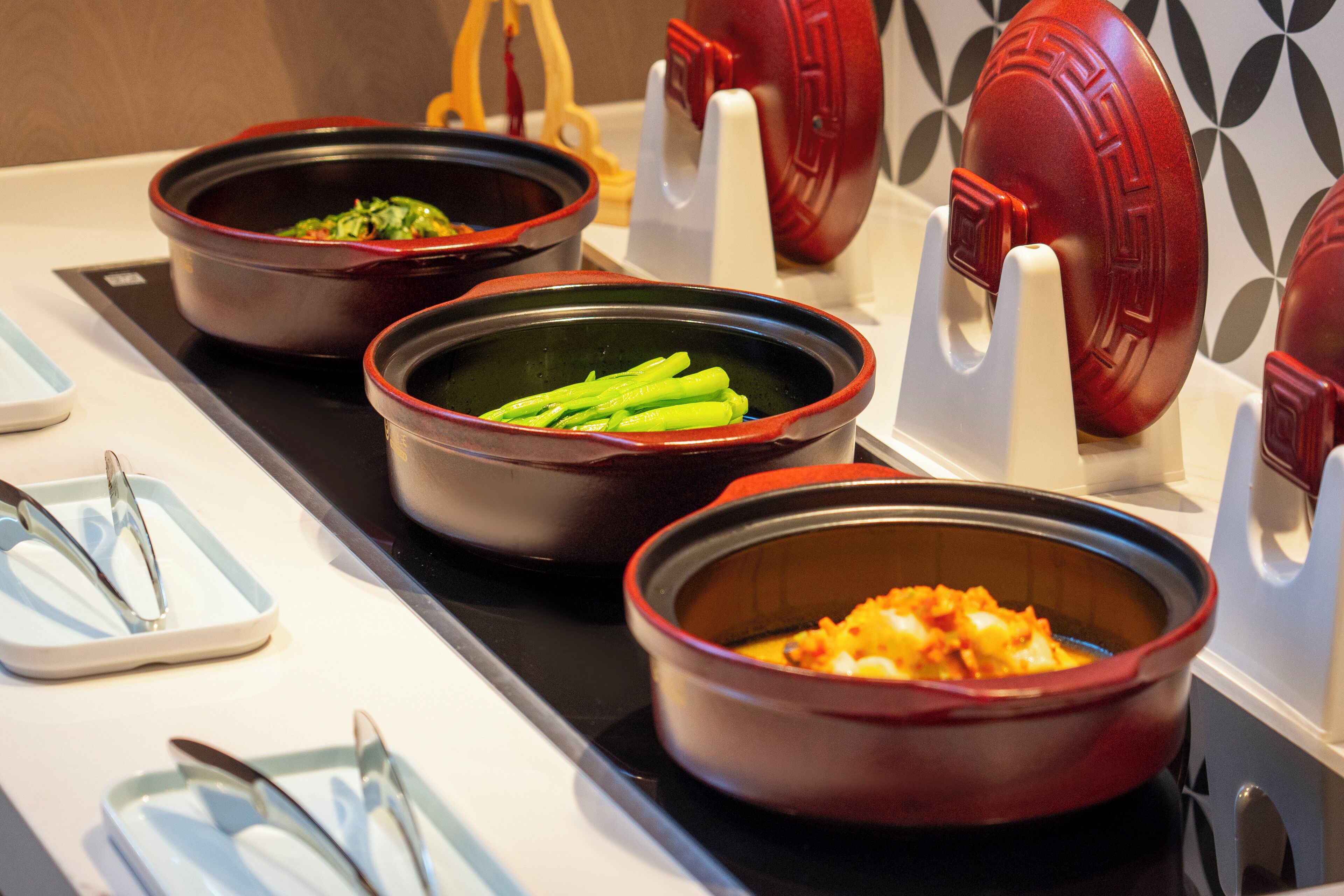 Montaje de bufé con diversos platos en recipientes de cerámica, dispuestos sobre una bandeja negra.
