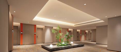 A spacious hotel lobby with a central garden feature, multiple doors, and a patterned carpet.