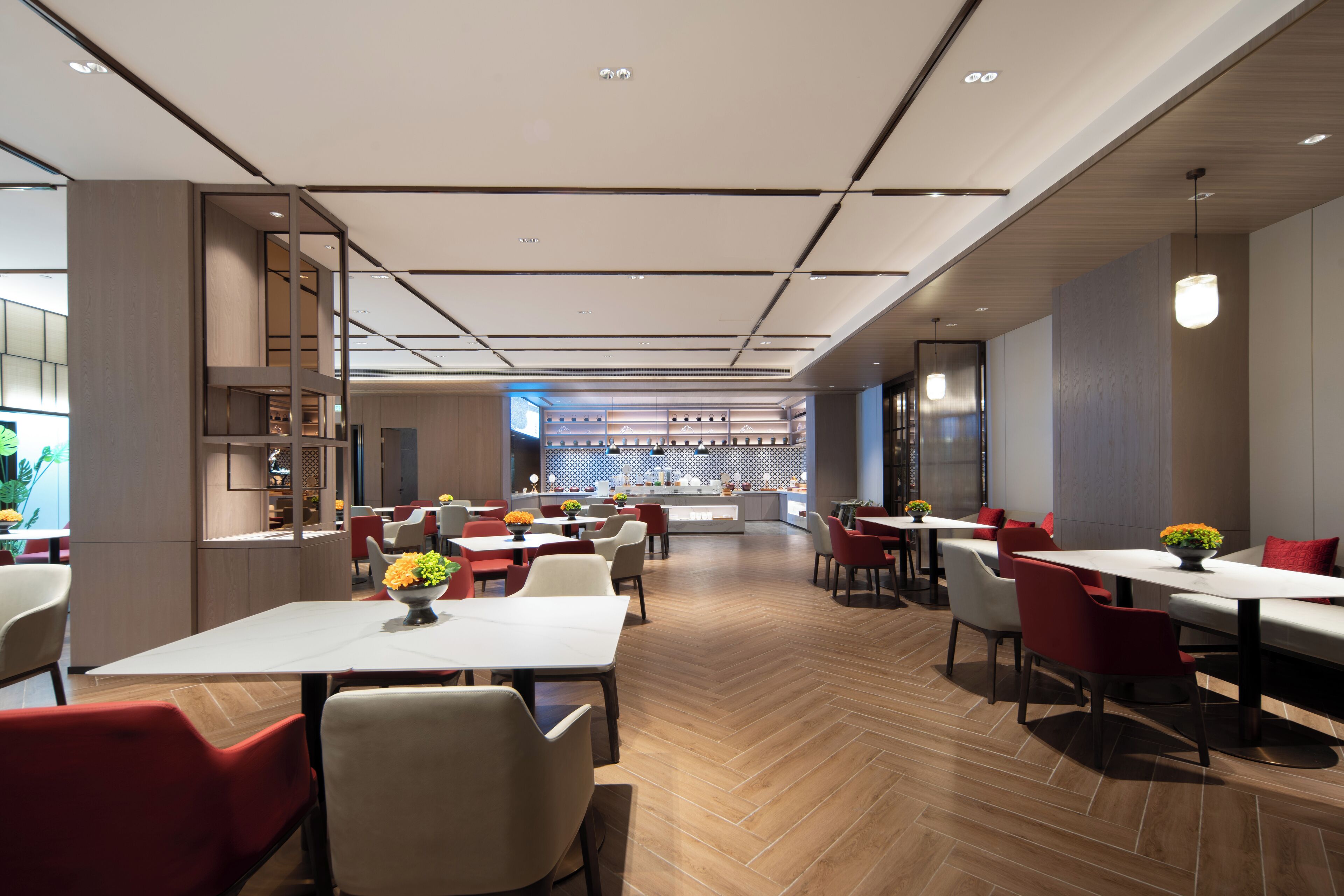A modern restaurant with a long counter, red and white chairs, and a herringbone wood floor.