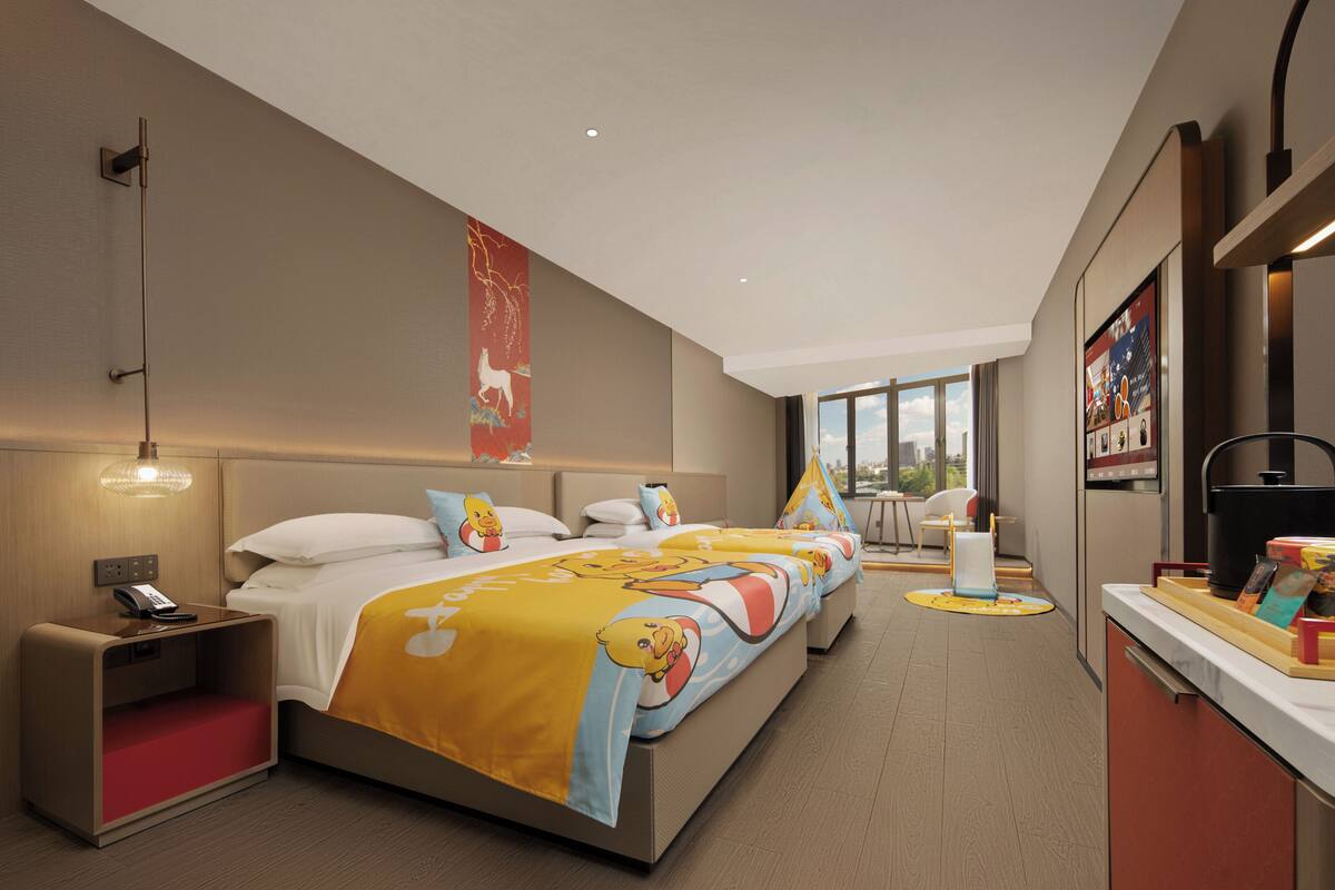 A modern hotel room with a large bed, bedside tables, a desk, and a view of the city.
