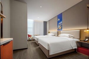 A hotel room with two beds, a desk, a chair, and a small table.