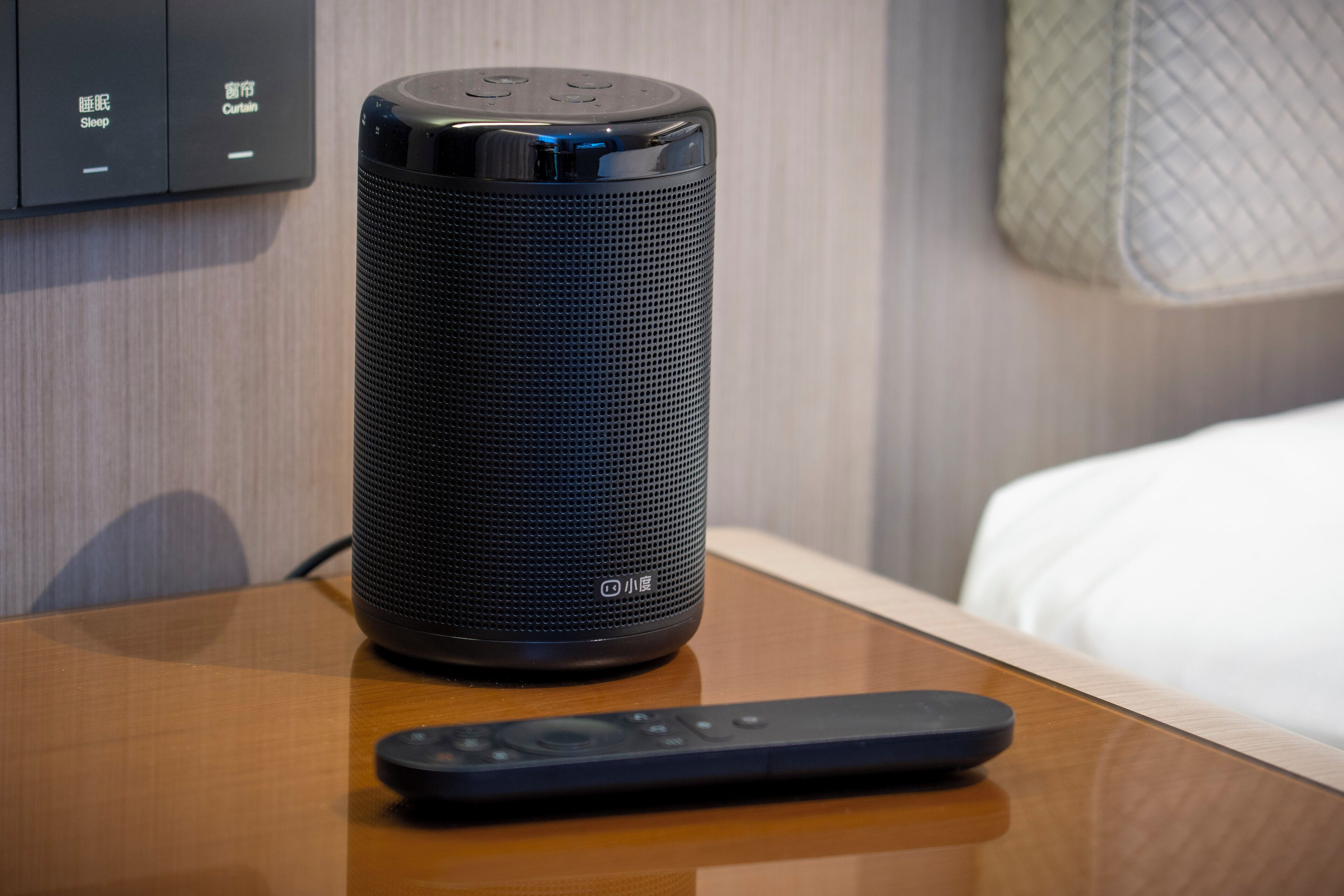 A black smart speaker on a wooden table with a remote control beside it.