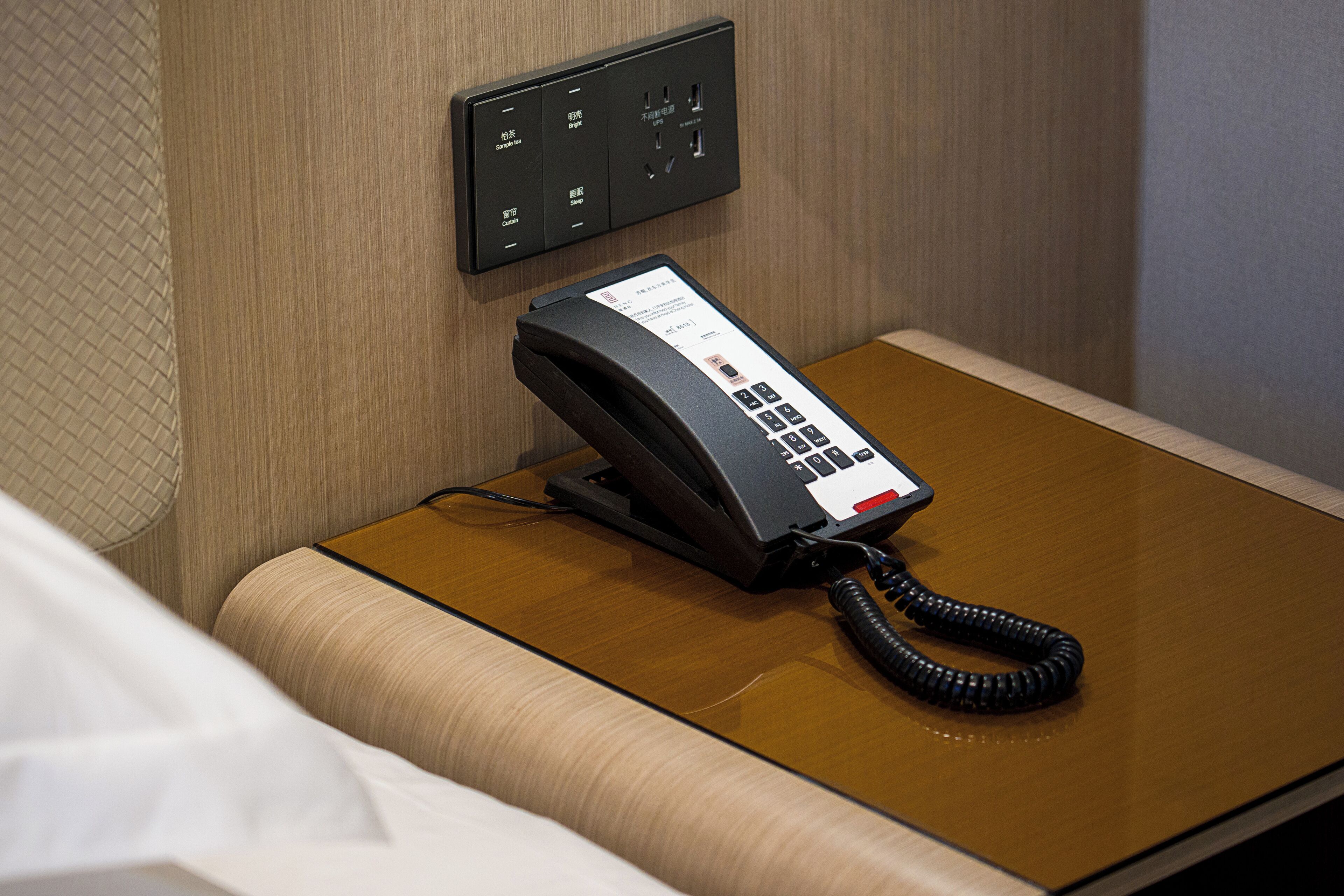Une chambre d’hôtel équipée d’un téléphone sur la table de chevet, d’une prise électrique et d’un panneau de commande au mur.