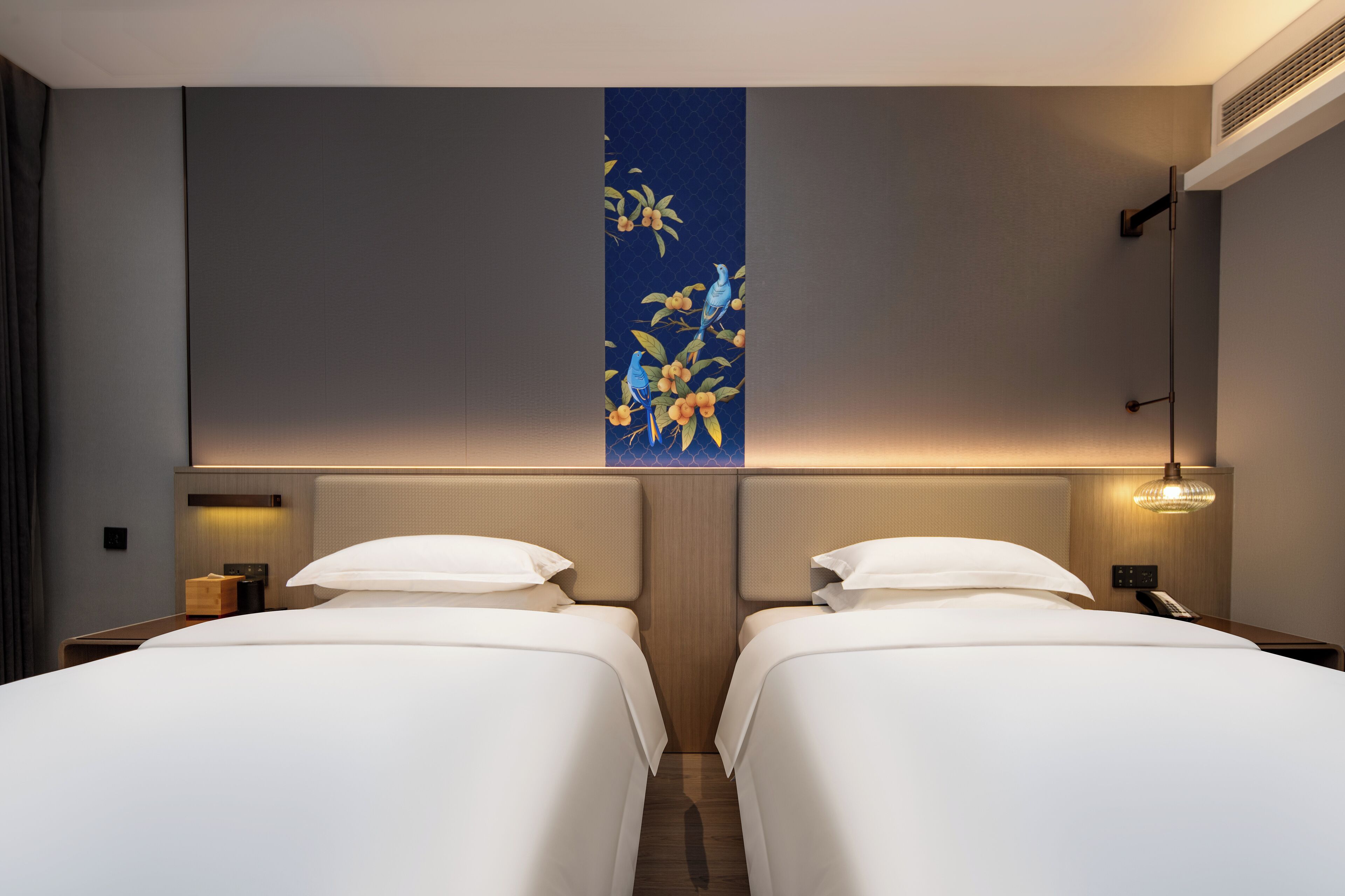 A hotel room with two beds, a wall-mounted artwork, bedside lamps, and a small table.