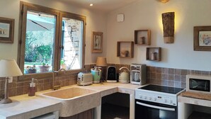 A kitchen with a wooden ceiling beam, a window with a view of greenery, a sink, a stove, and a microwave. - Le Mas Natán Au Coeur du luberon Gordes (Gordes)