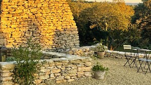 A stone structure with a curved wall, surrounded by gravel and potted plants, with trees and a clear sky in the background. - Le Mas Natán Au Coeur du luberon Gordes (Gordes)