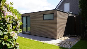 A modern house with a wooden exterior, a glass door, and a small garden area with a gravel path. - "Das Vosshörn - Steuermann" - designer vacation apartment with two terraces (Cuxhaven)