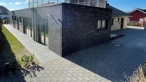 A modern building with a glass facade, a metal balcony, and a paved courtyard. - "Das Vosshörn - Steuermann" - designer vacation apartment with two terraces (Cuxhaven)